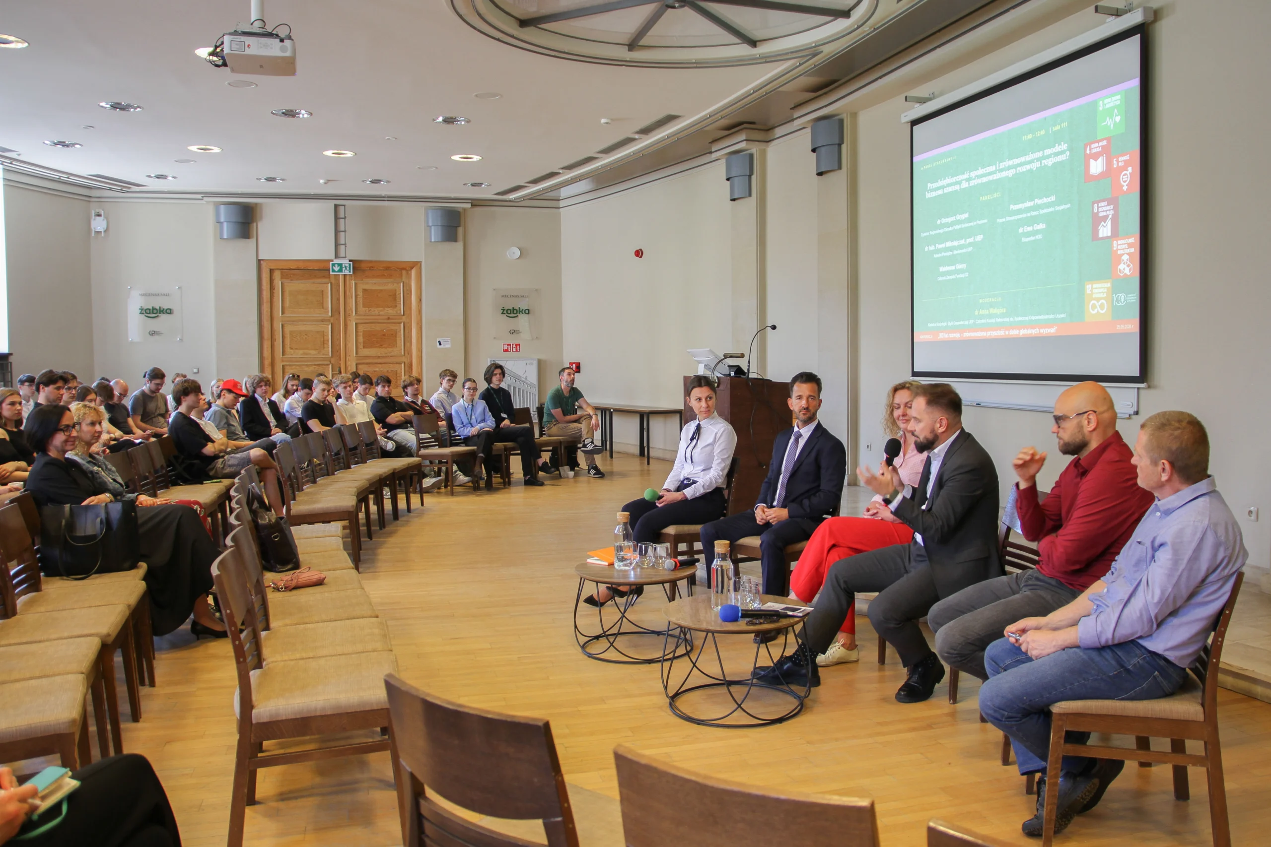 Grupa prelegentów prowadzi panel dyskusyjny przed publicznością w sali konferencyjnej, z wyświetlanym na ekranie tematem o zrównoważonym rozwoju regionu.